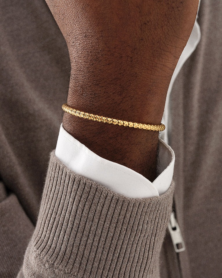 A polished stainless steel bangle in 14k gold plated from Waldor & Co. One size. The model is Noble Bangle Polished