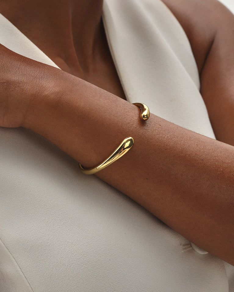 A polished stainless steel bangle in 14k gold from Waldor & Co. One size. The model is Teardrop Bangle Polished
